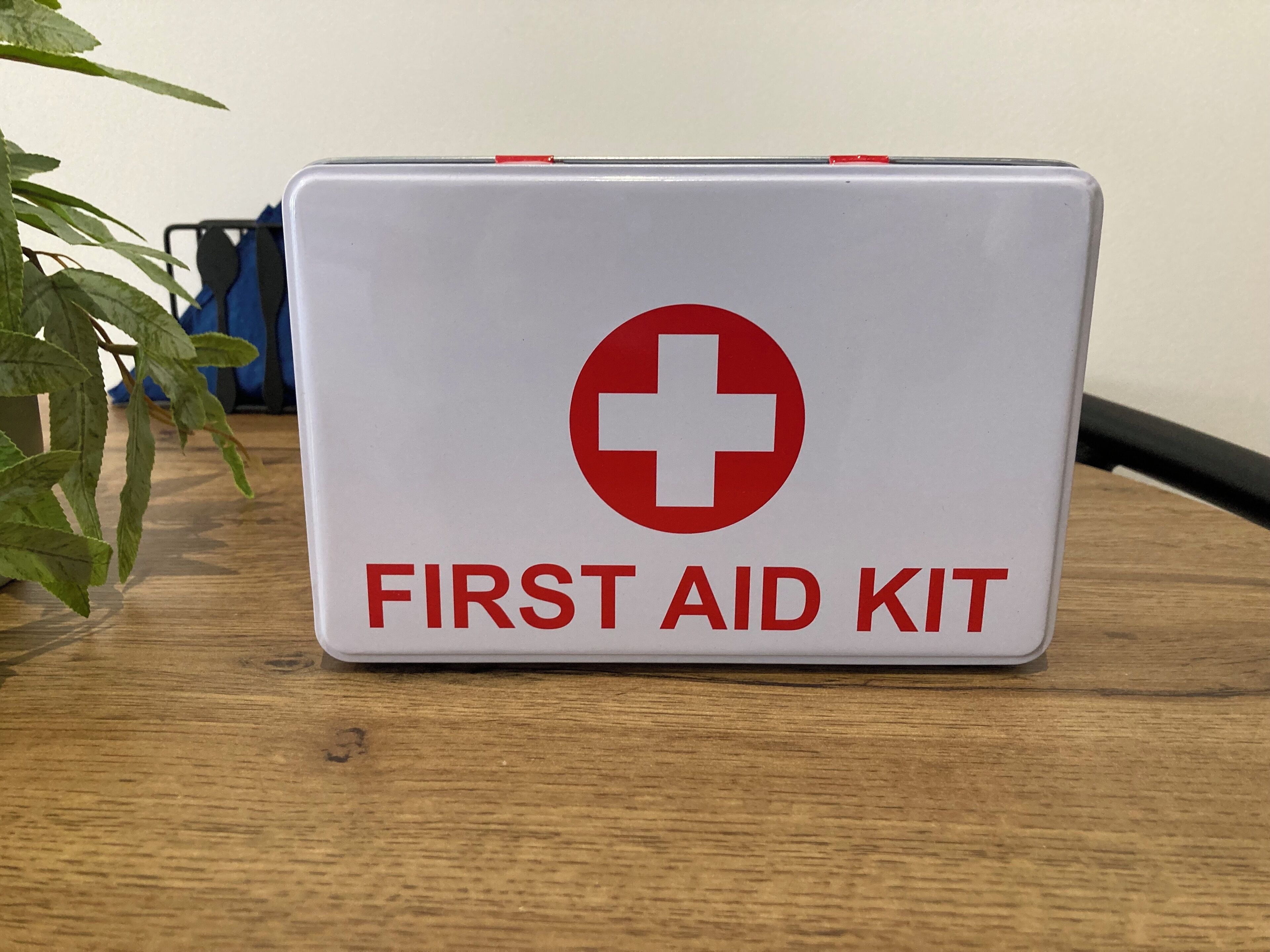 A white first aid kit with a red cross symbol and the text "FIRST AID KIT" on a wooden surface.
