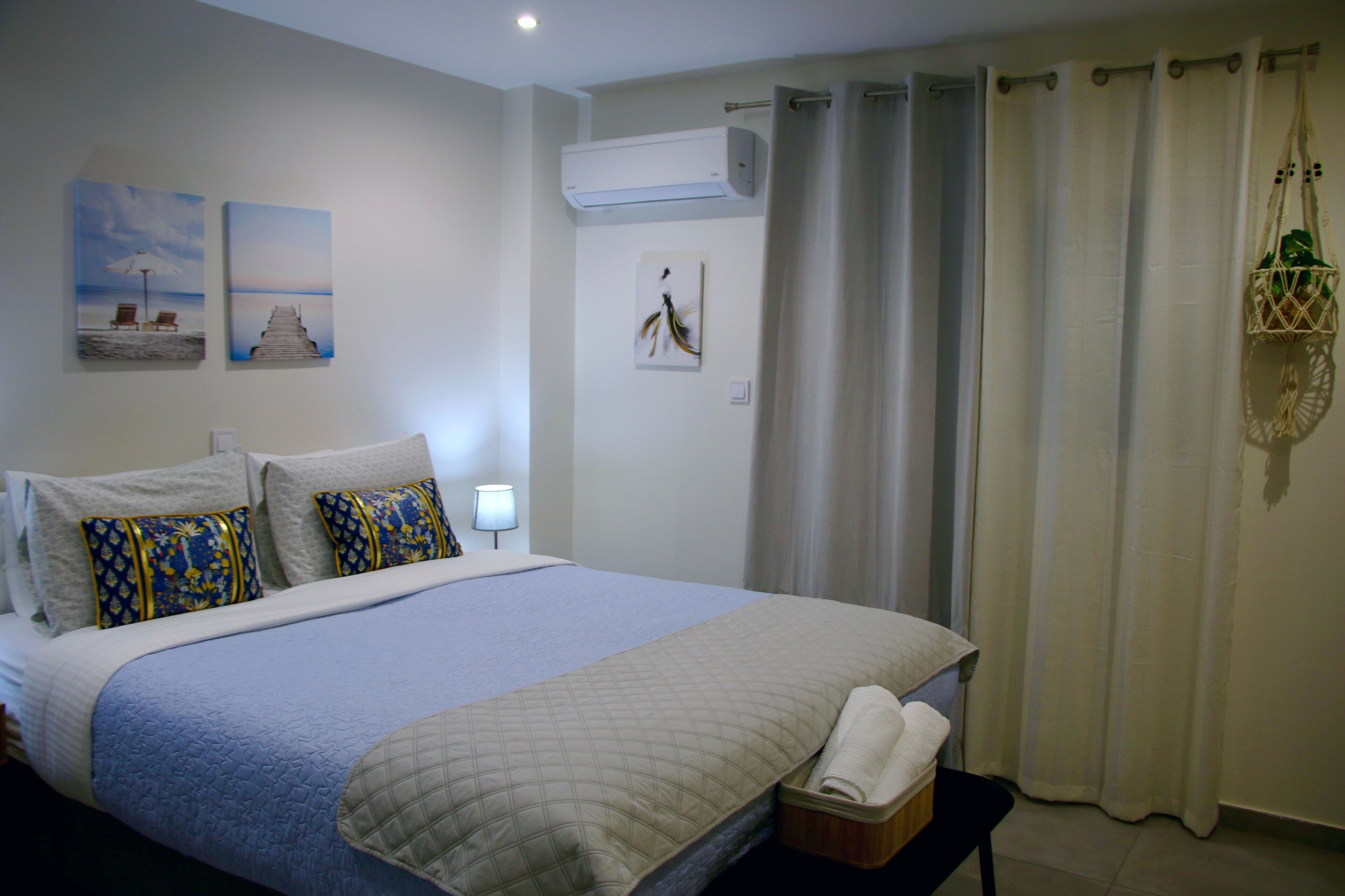 A neatly made bed with a quilted blanket and decorative pillows, a bedside lamp, and artwork on the wall.