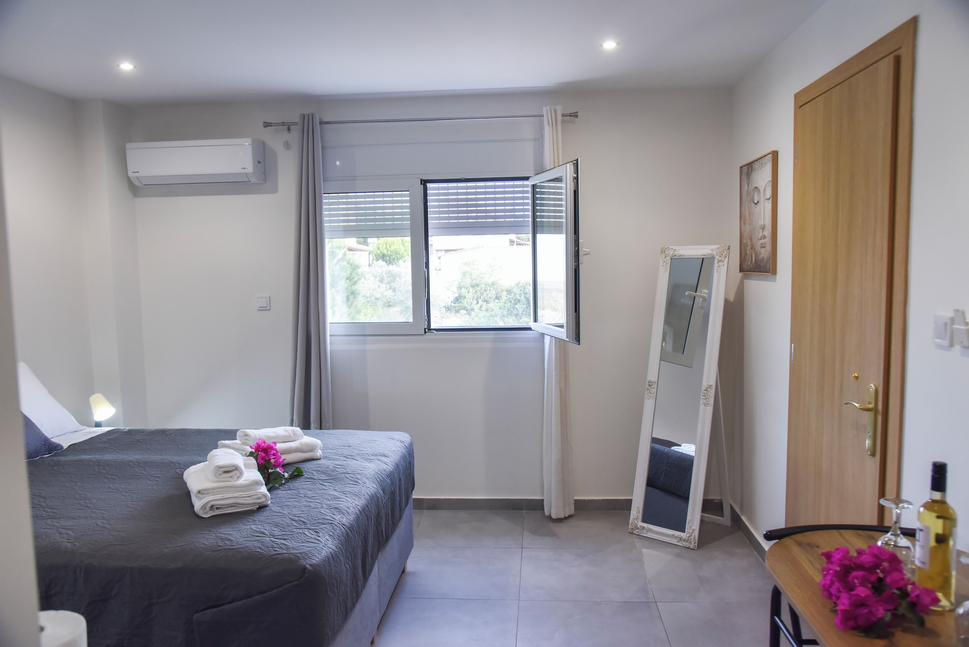 Een hotelkamer met een bed, nachtkastje met toiletartikelen, een spiegel en een raam met zonwering.