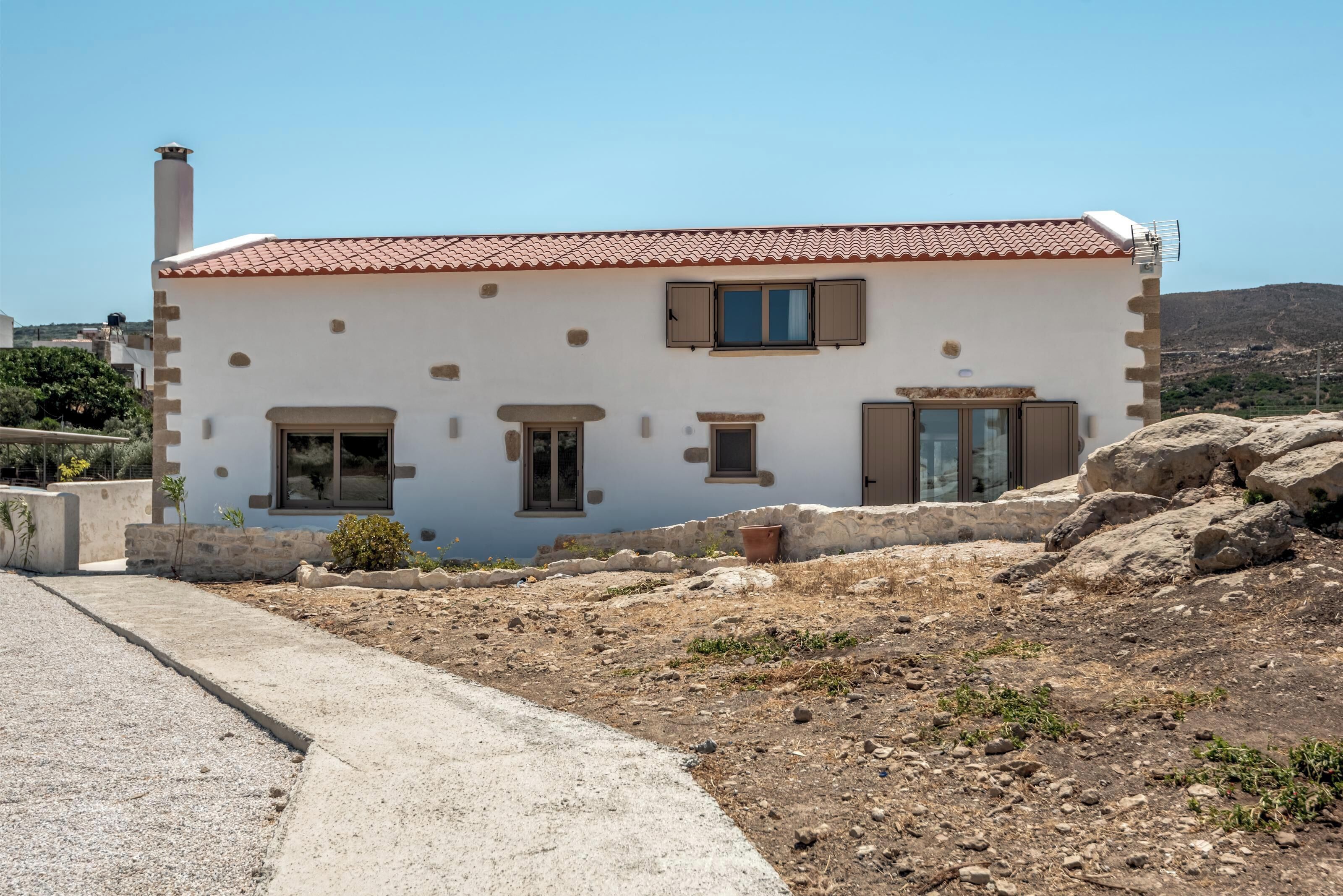 A two-story building with a red-tiled roof, stone walls, and multiple windows.