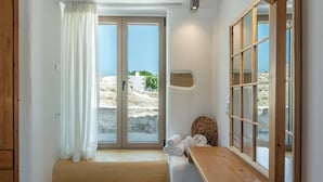 A bathroom with a wooden bench, a towel rack with towels, a large window with a view of the beach, and a wooden door. - Villa Froudi (Kissamos)