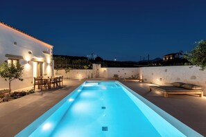 A swimming pool with a sunken seating area, surrounded by a patio with outdoor furniture and a stone wall. - Villa Froudi (Kissamos)