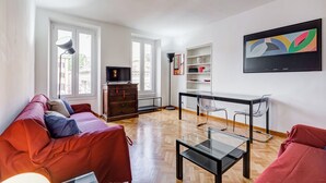 A modern living room with a sofa, a glass-top coffee table, a TV, and a bookshelf. - Luminous Apartment few steps P.za Navona (Rome)