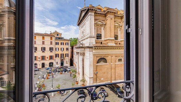 A view from a window overlooking a street with historic buildings, a cobblestone street, and parked cars. - Luminous Apartment few steps P.za Navona (Rome)