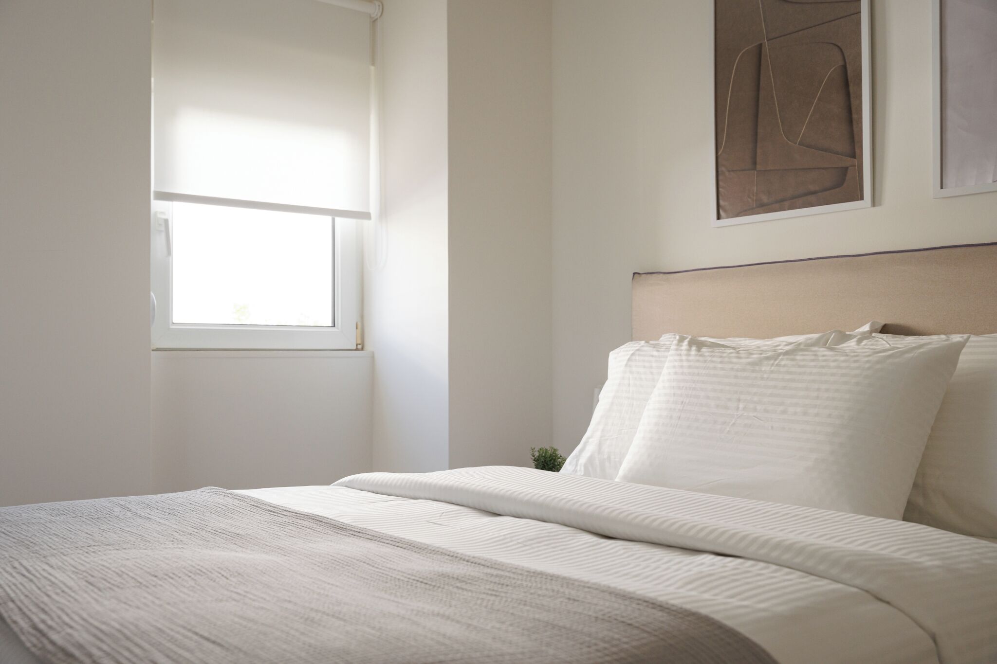 A bedroom with a bed, a window, and a wall-mounted artwork.