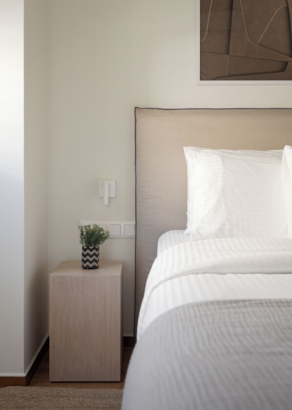 A neatly arranged bedroom with a bed, a bedside table with a potted plant, and a wall-mounted light fixture.