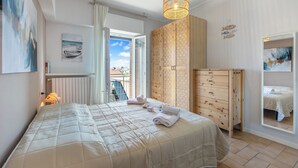 Una camera da letto con un letto, un armadio in legno, una lampada a sospensione e vista attraverso una porta aperta.