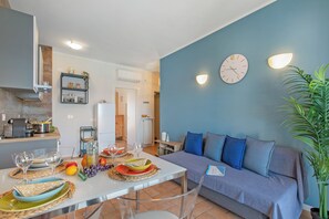 A modern living room with a sofa, a dining table with plates and glasses, a clock, and a wall-mounted light fixture. - Maderno Sweet Home (Toscolano Maderno)