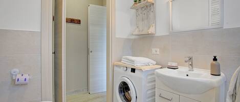 A modern bathroom with a washing machine, a sink, and a mirror.