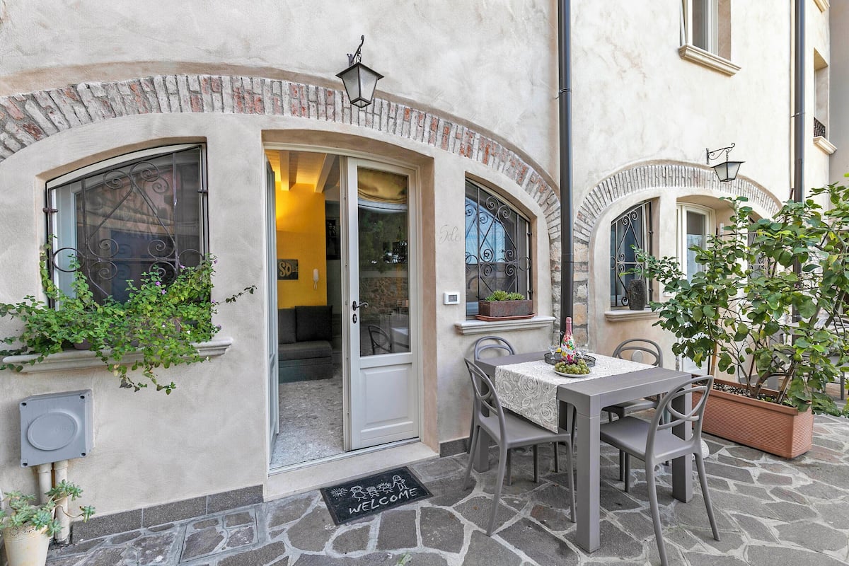 An outdoor seating area with a table and chairs, a door with a 'For Sale' sign, and potted plants.