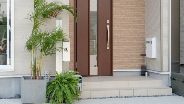 Una entrada moderna de edificio con puerta de vidrio, planta en maceta y un escalón que conduce a la entrada.