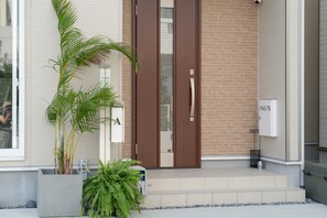 Ein moderner Gebäudeeingang mit Glastür, Blumentopf und einer kleinen Stufe zum Eingang.
