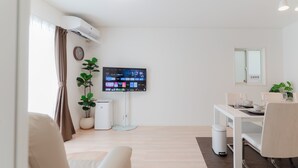 Una sala moderna con televisor de pantalla plana, una mesa de comedor, sillas, un sofá, una planta en maceta y un cubo de basura.