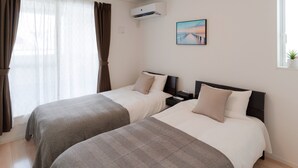 Habitación de hotel con dos camas, una ventana con cortinas, un aire acondicionado, una mesita de noche y un cuadro en la pared.