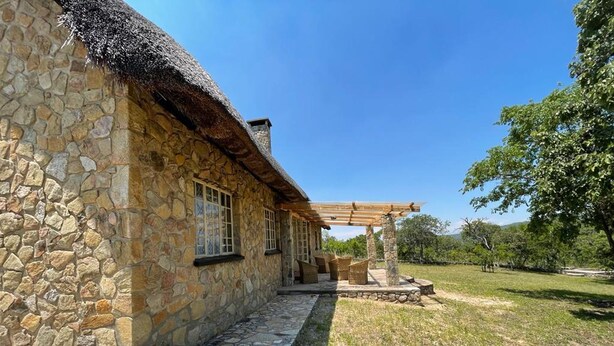A stone building with a thatched roof, a covered outdoor seating area, and a stone pathway leading to the entrance. - Lovely 3 bed House in Juliasdale - 2273 (Nyanga)