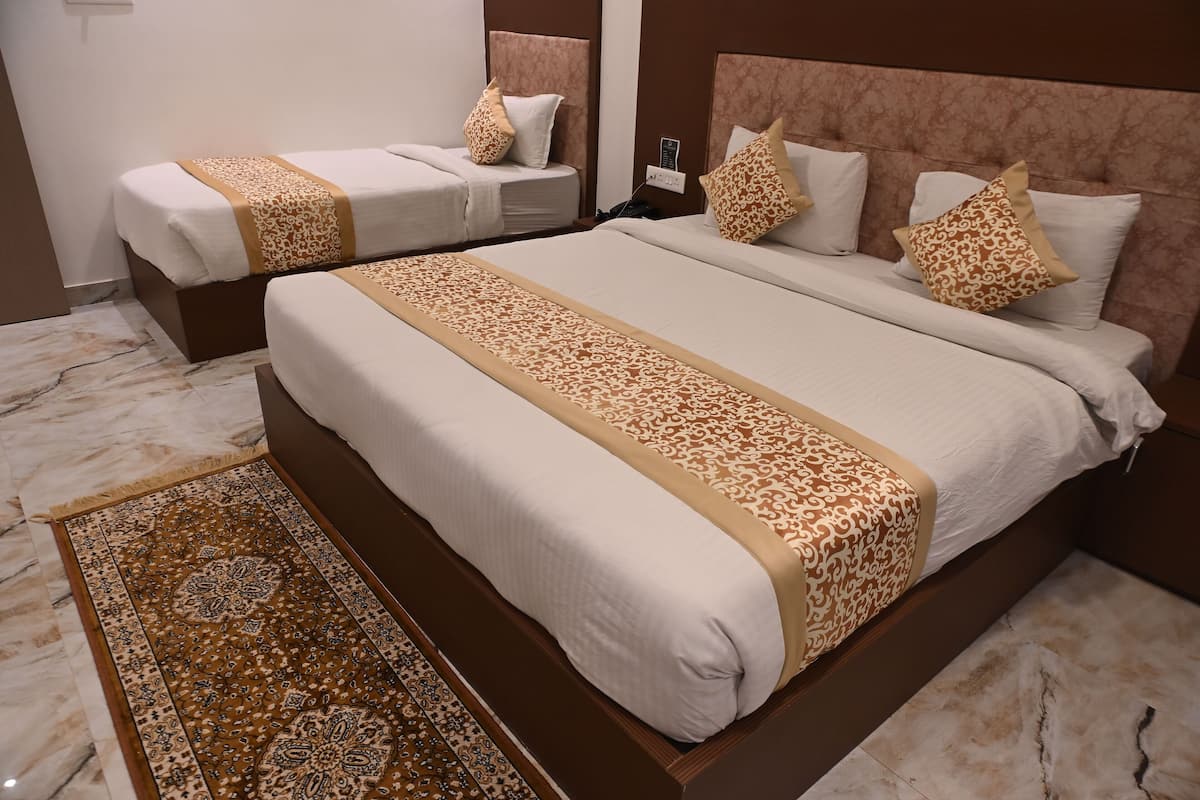 A hotel room with two beds, a large bed with a patterned bedspread and a smaller bed with a plain bedspread.