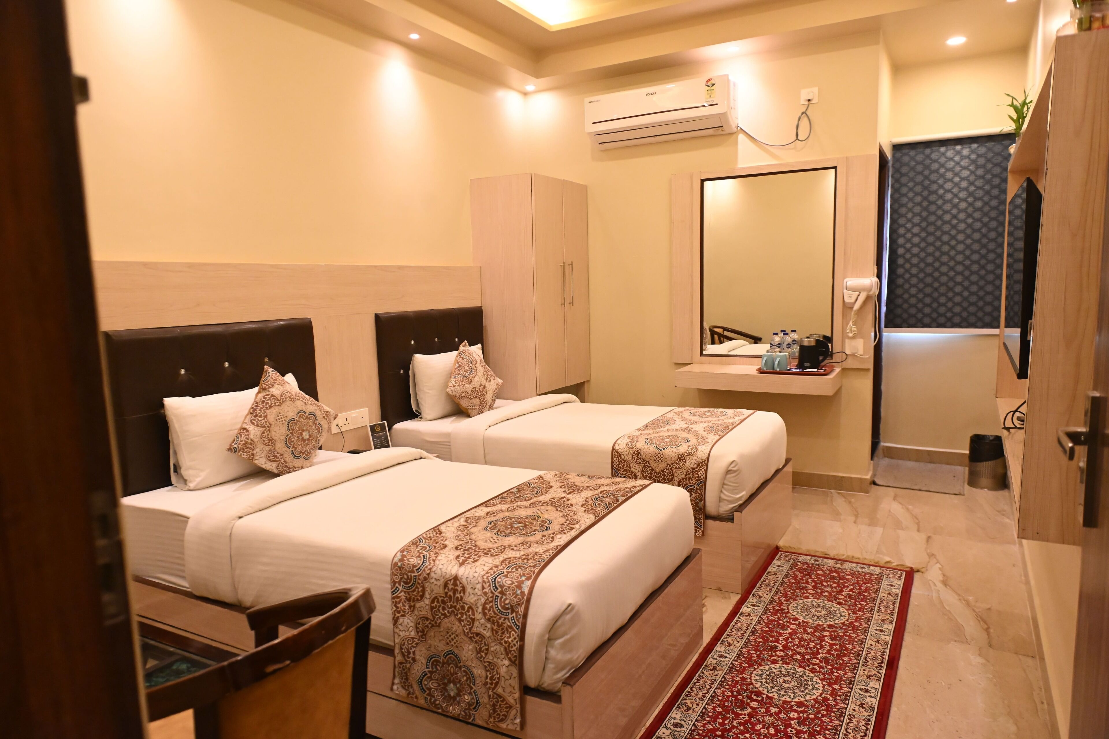 A hotel room with two beds, a wardrobe, a mirror, an air conditioning unit, and a small bathroom area.