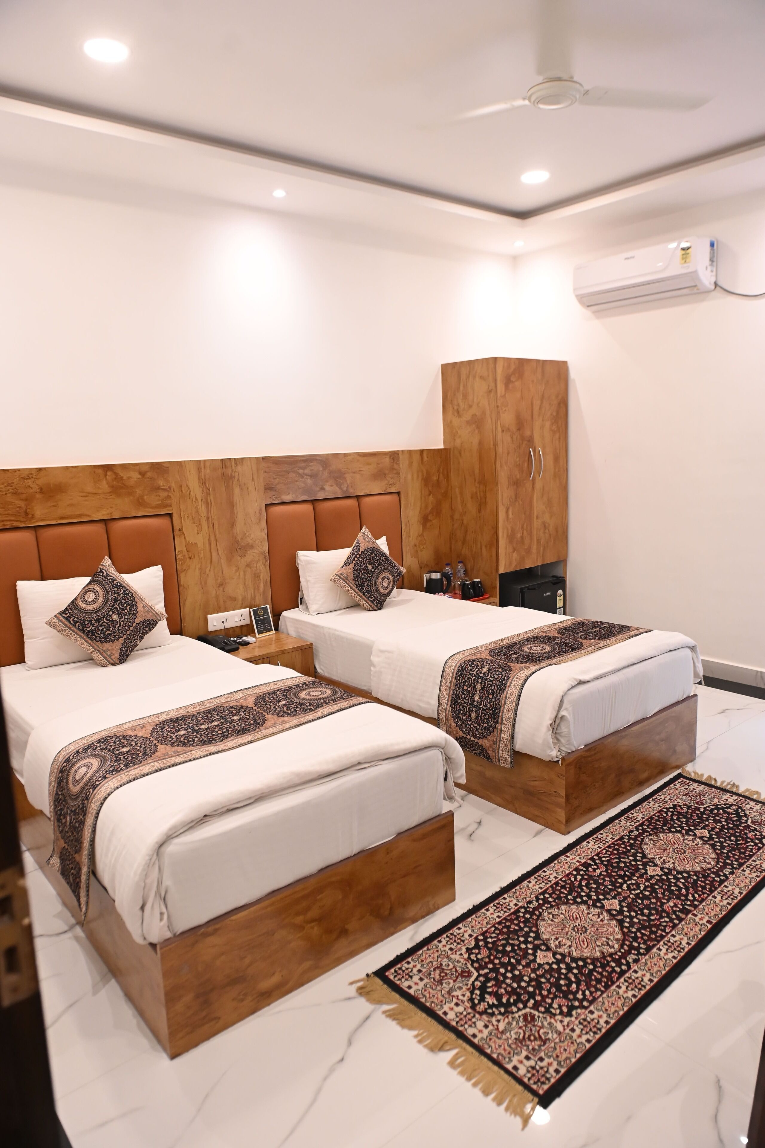 A hotel room with two beds, a wooden headboard, a large rug, and an air conditioning unit.
