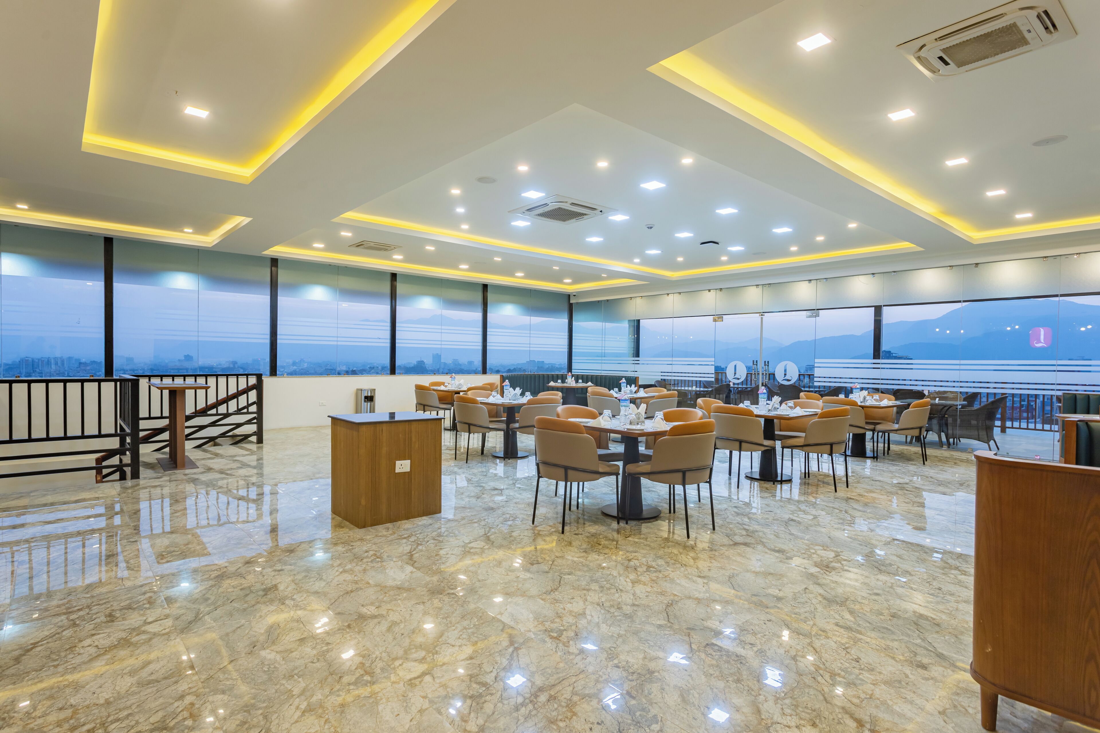Un'ampia sala da pranzo con diversi tavoli e sedie, pavimento in marmo e grandi finestre con vista sulla città.