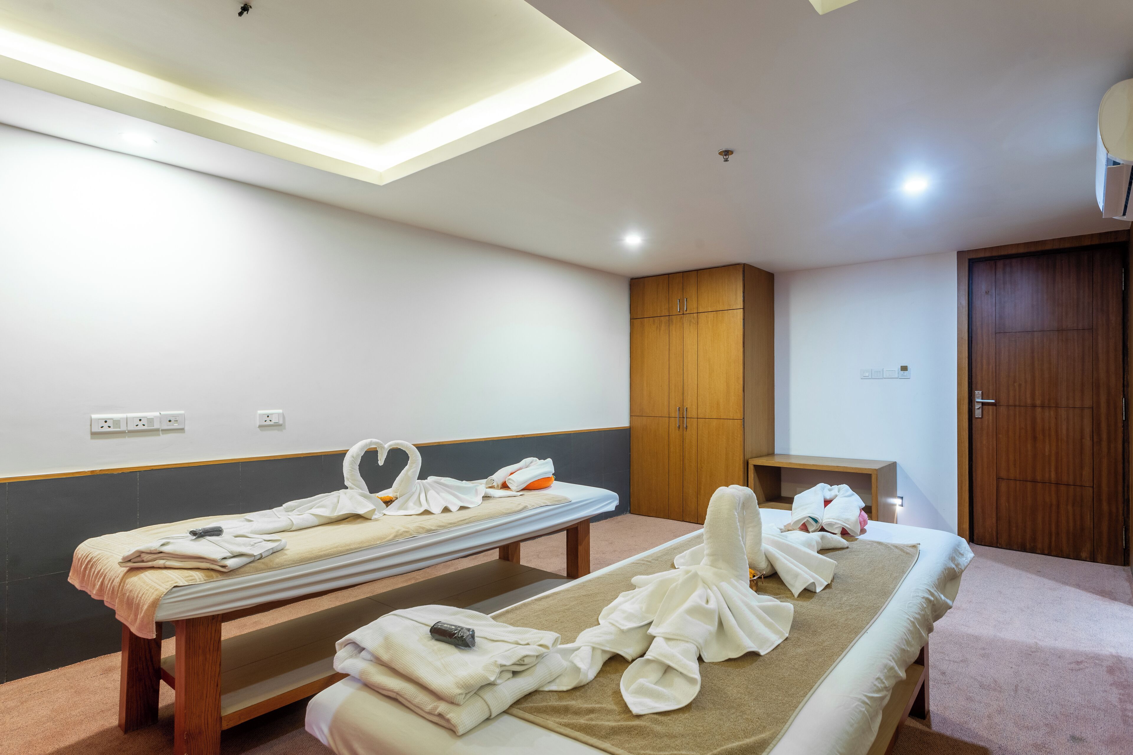 A room with two beds, a wooden cabinet, a small table, and a ceiling light fixture.