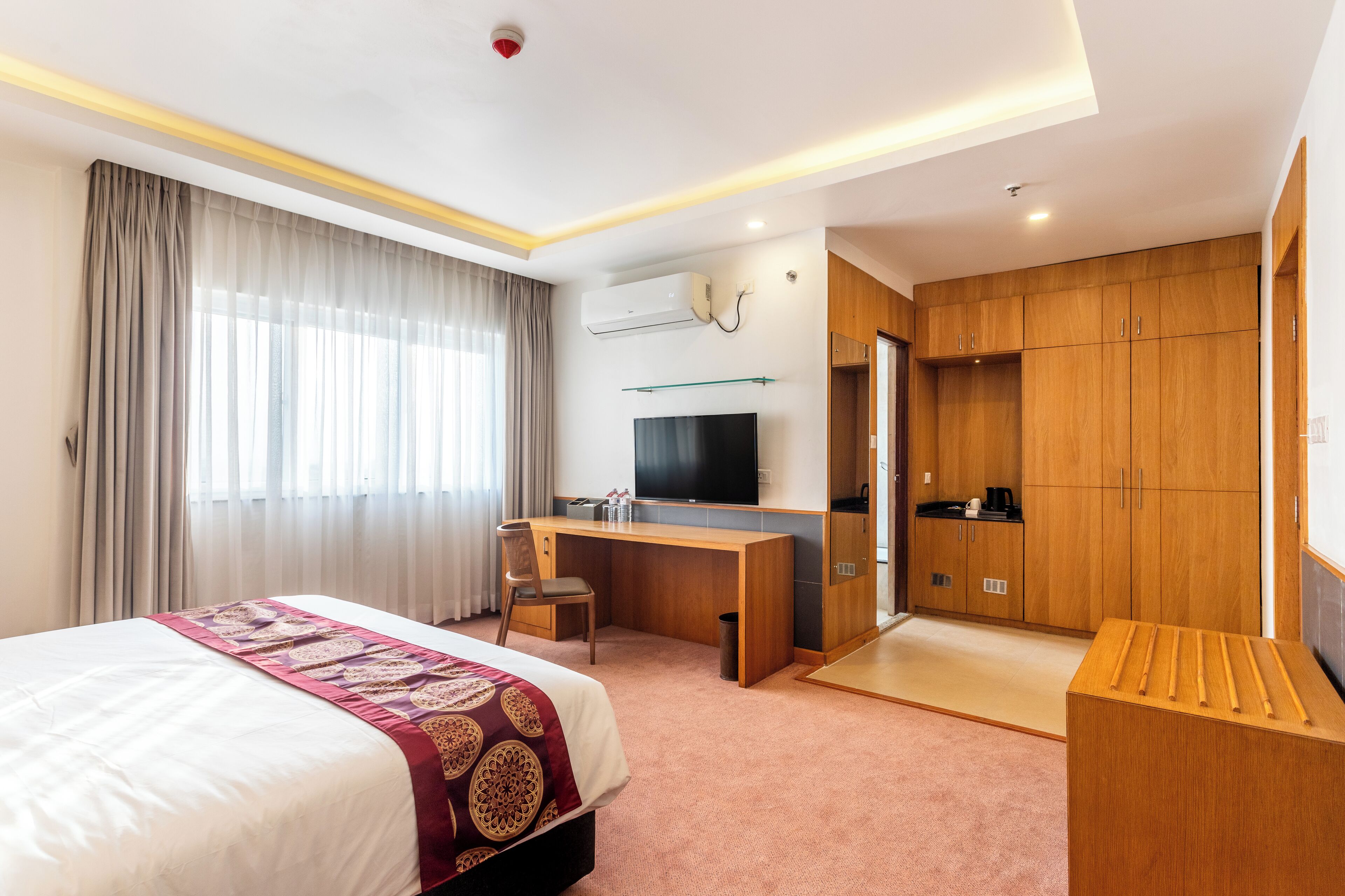 A hotel room with a bed, desk, TV, wardrobe, and a small table.