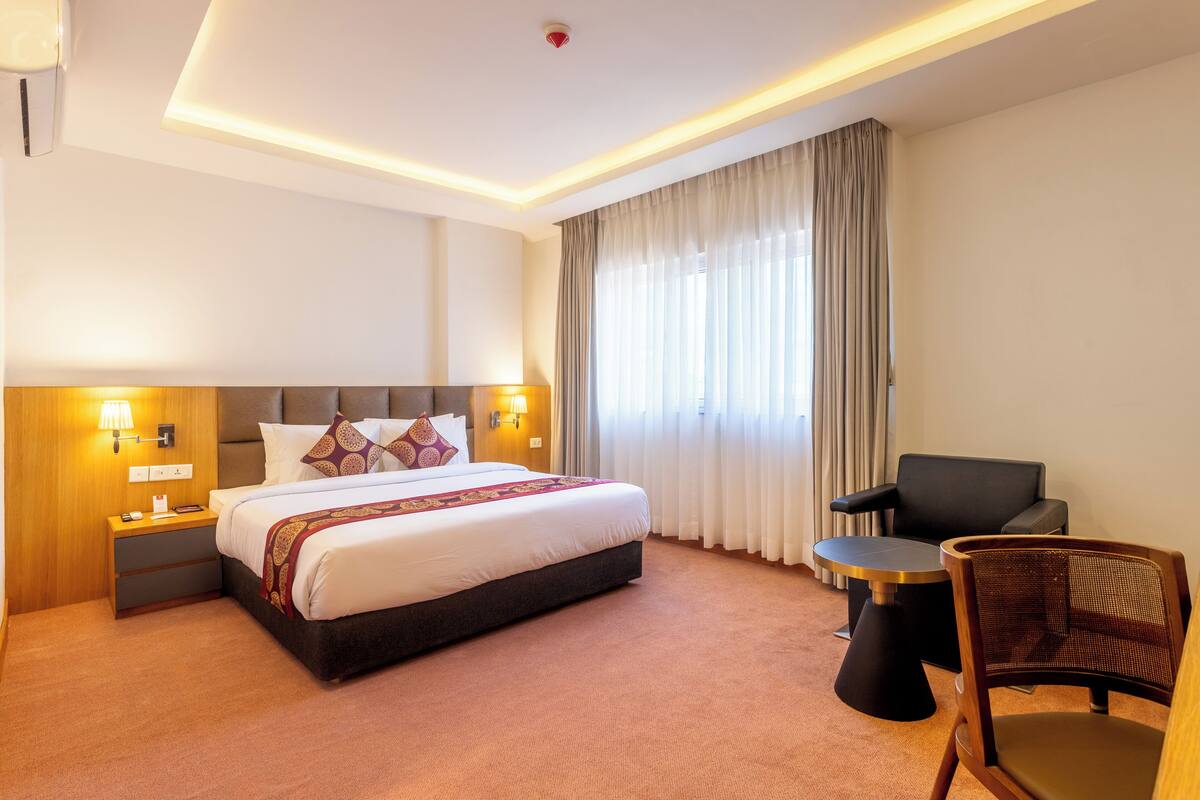 Una habitación de hotel con una cama grande, mesitas de noche, una silla y una pequeña mesa.
