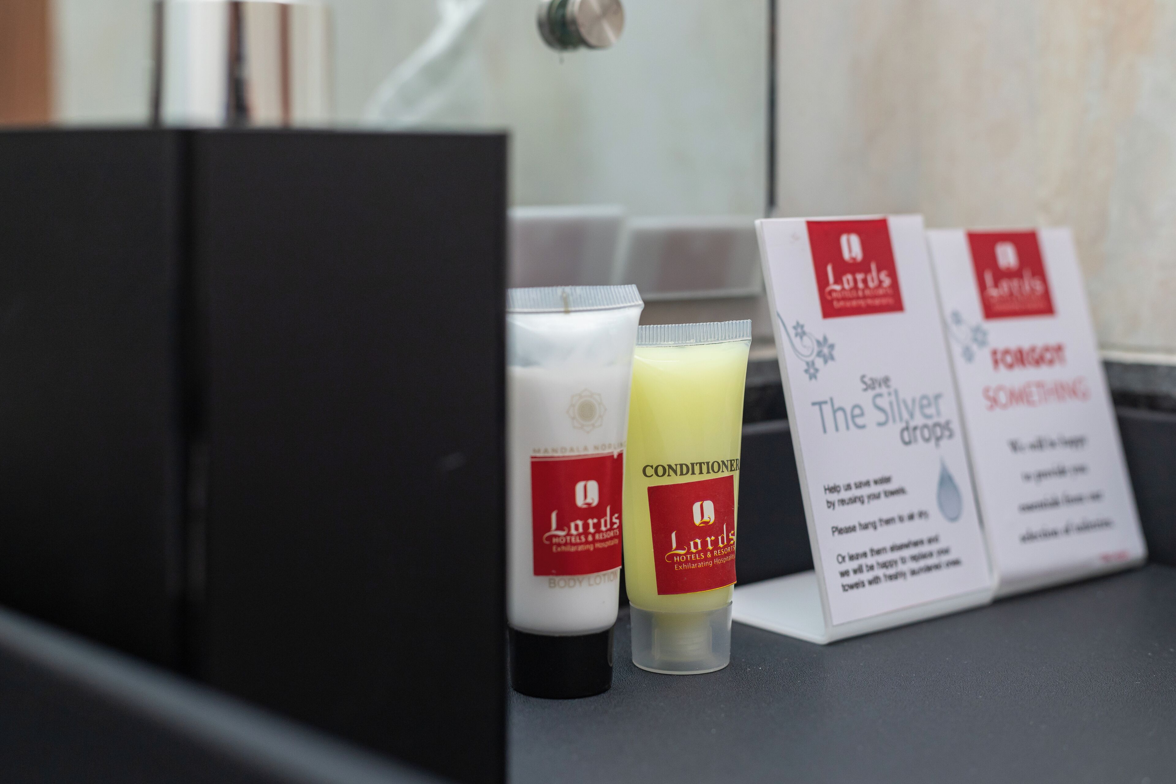 A hotel bathroom with toiletries including body lotion, conditioner, and a sign promoting water conservation.