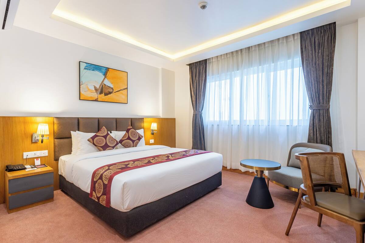 Una habitación de hotel con una cama grande, lámparas de noche, una mesita y una silla.