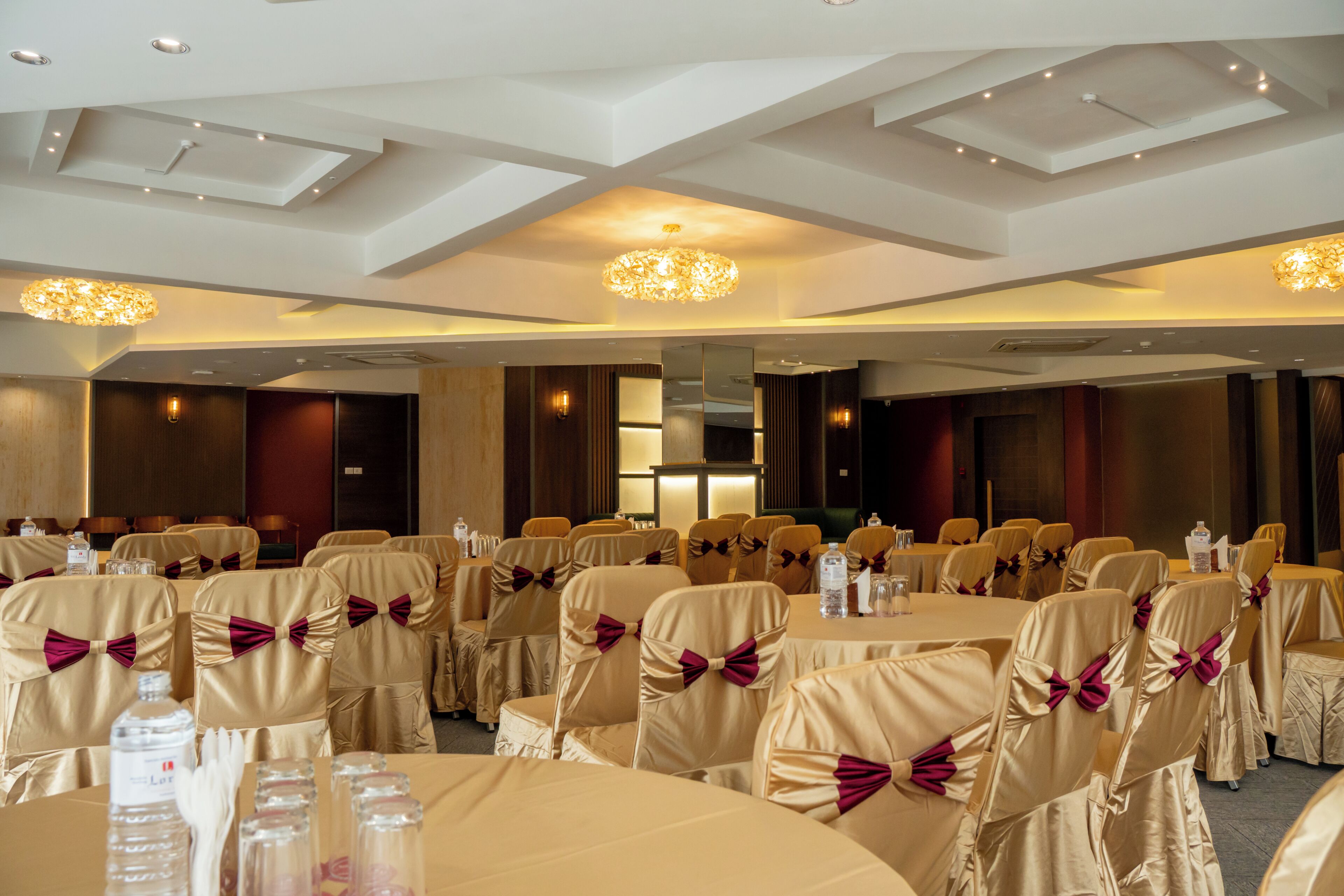A banquet hall with round tables, chairs with bow ties, and a modern chandelier.