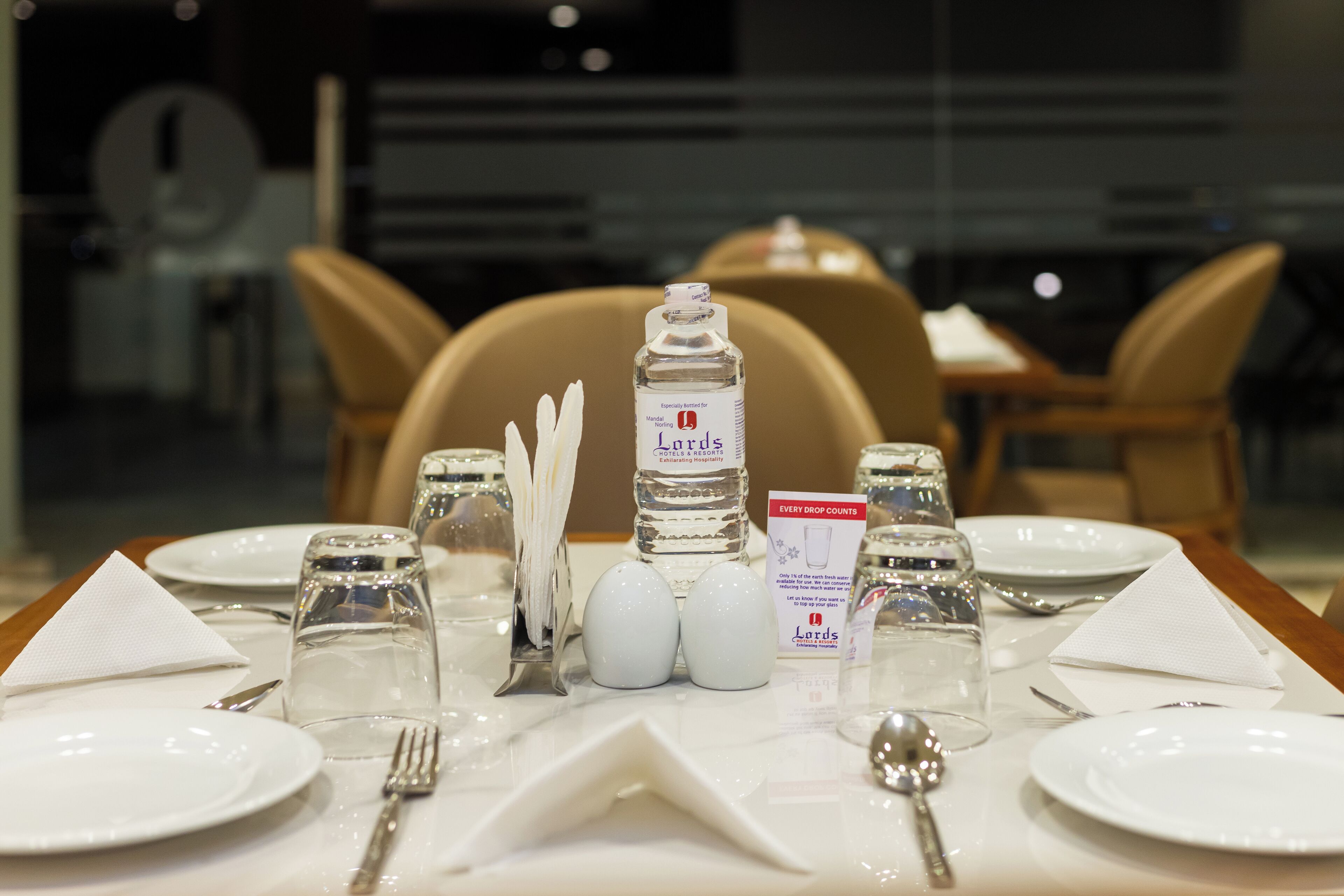Une table à manger dressée avec de l’assiette blanche, des couverts en argent et une bouteille d’eau portant l’étiquette « Lords ».