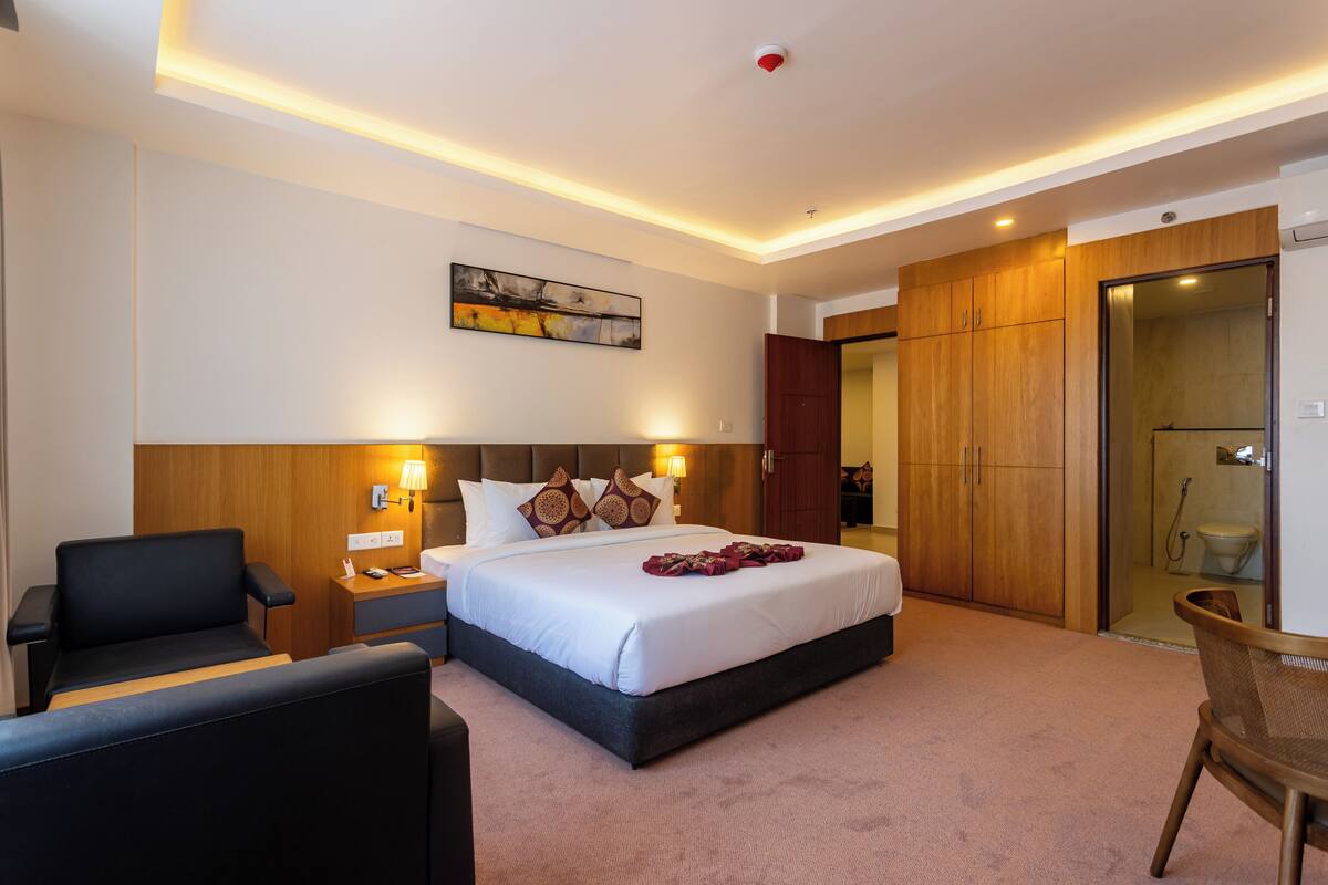 Una habitación de hotel con cama, mesitas de noche, una silla, un cuadro en la pared y un armario.