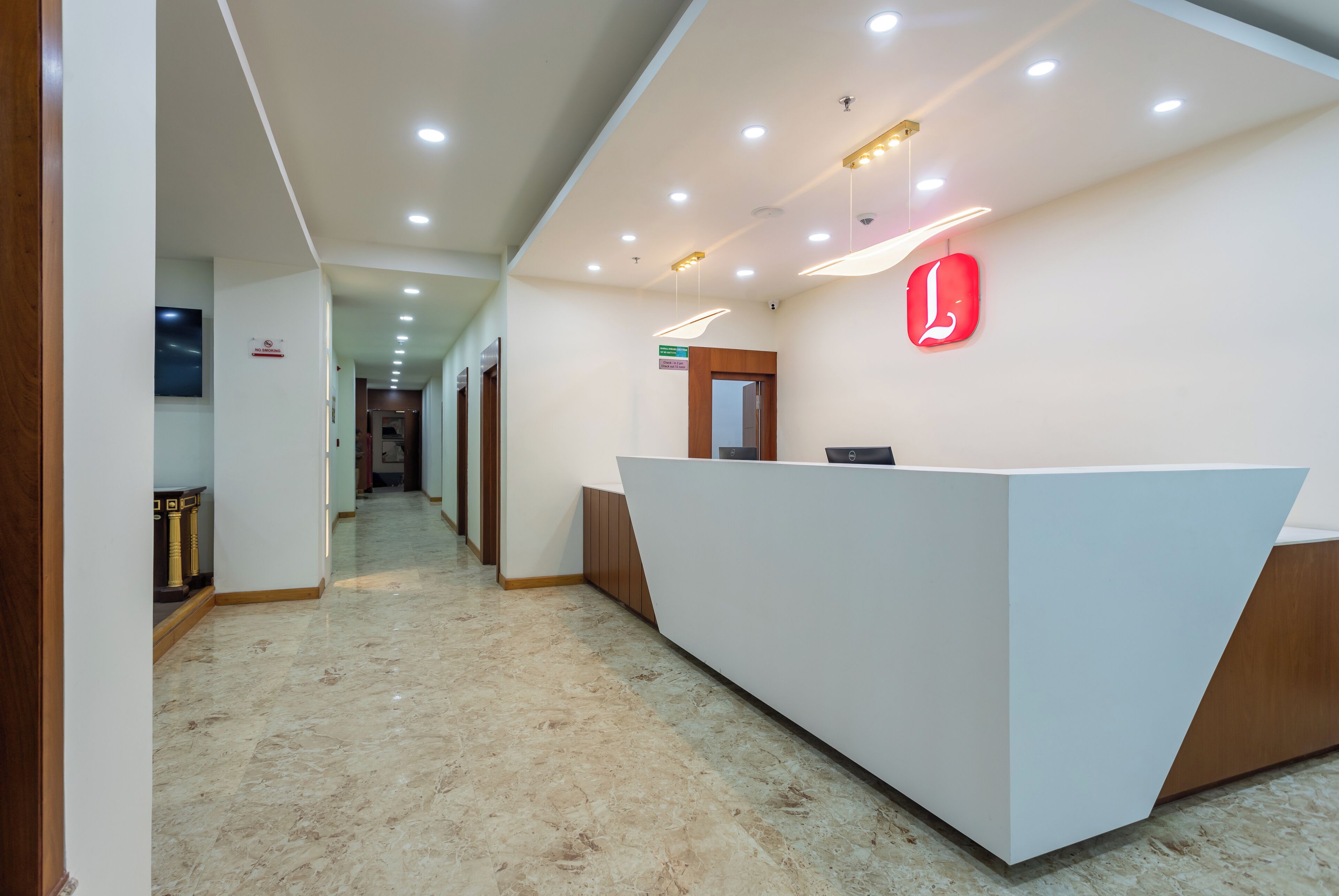 A modern reception area with a white reception desk, a red logo on the wall, and a marble floor.