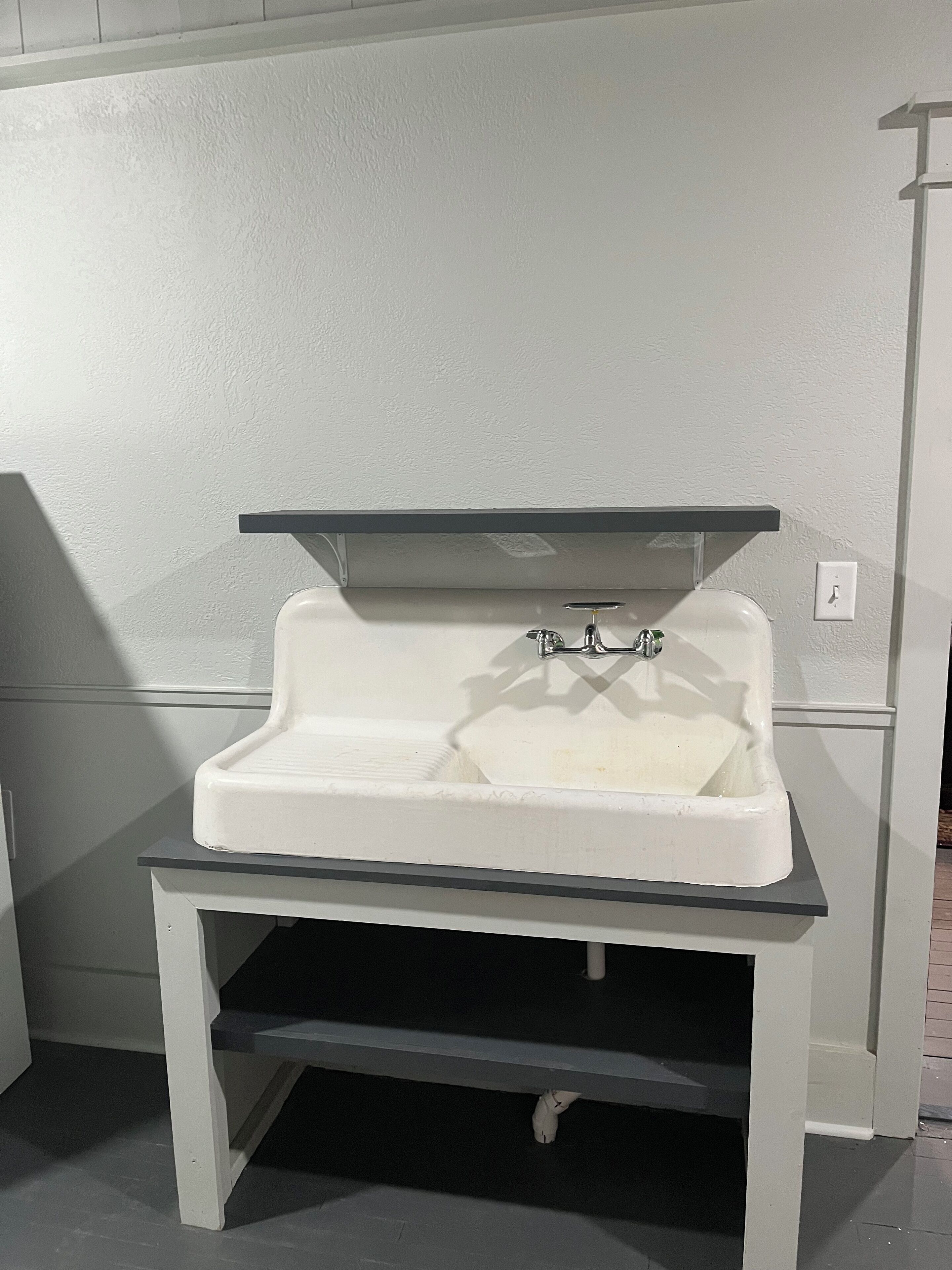 A white pedestal sink with a black countertop and a shelf above it.