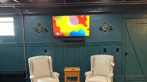 A room with a large flat-screen TV mounted on the wall, two armchairs, a small wooden side table, and a leather sofa.