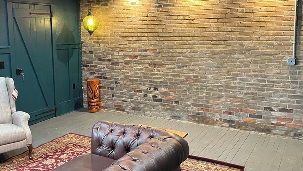 A room with a brick wall, a leather sofa, a patterned rug, and a teal door.