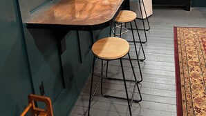 A room with a long table, wooden stools, and a window with natural light.