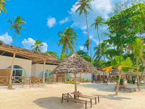 A beach resort with thatched-roof structures, palm trees, and outdoor seating areas.
