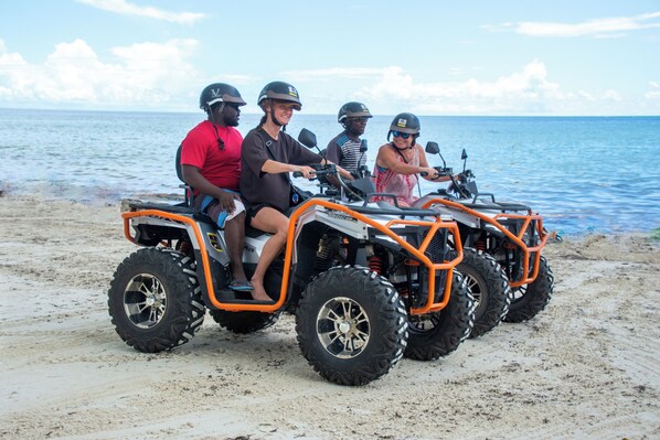 Four people on an ATV on a sandy beach with the ocean in the background.