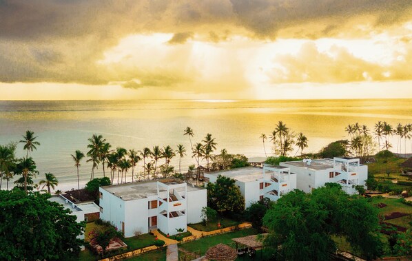 A coastal resort with white buildings, palm trees, and a view of the sea.