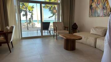 Amplia sala de estar con un gran ventanal corredizo que da a vista de playa, un sofá color beige, dos sillones y una mesa de centro de madera.