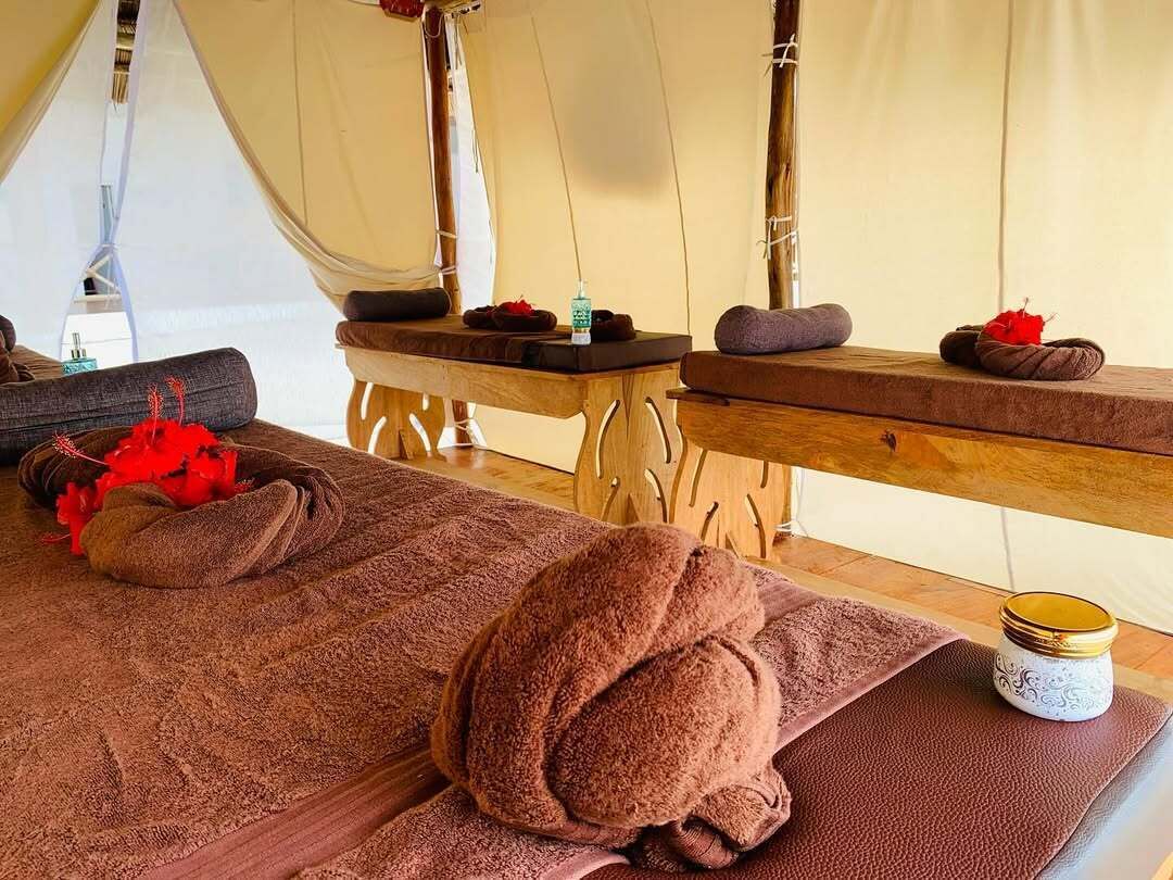 A massage room with two wooden massage tables, towels, and a decorative jar.