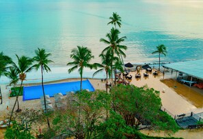 A beachside hotel with a pool, palm trees, and a view of the ocean.