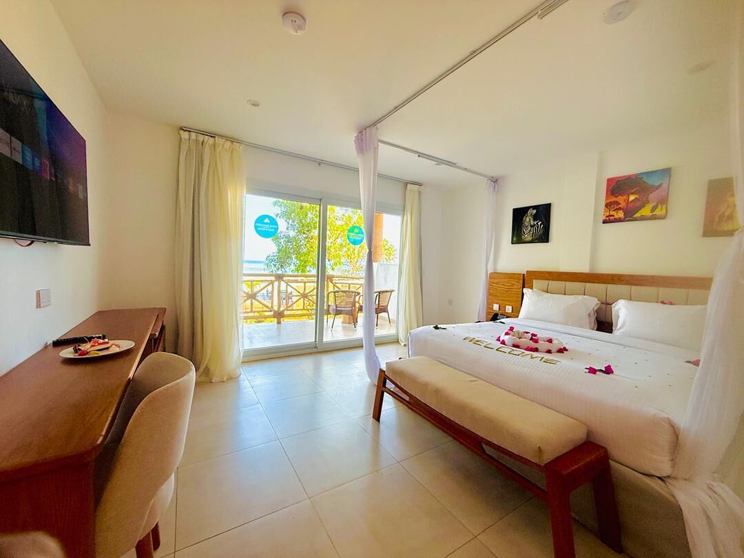 A hotel room with a bed, a desk, and a balcony with a view of trees.