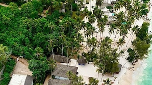 Vue aérienne d’un complexe hôtelier avec des bungalows aux toits de chaume, un espace piscine et une plage.