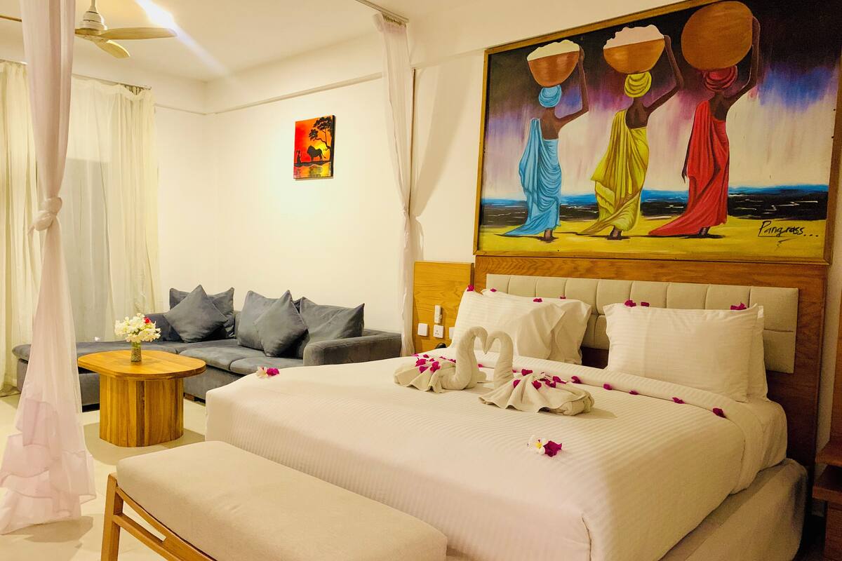 A hotel room with a large bed, a sofa, a small round table, and a painting on the wall.