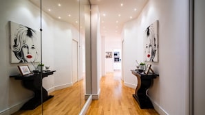 A hallway with wooden flooring, mirrored walls, and artwork on either side.