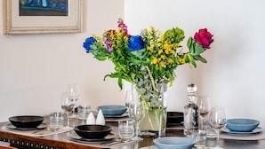 A dining table set with blue plates, black bowls, and clear glasses, with a vase of colorful flowers in the center.