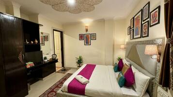 A hotel room with a large bed, a television, a desk, and a wardrobe.