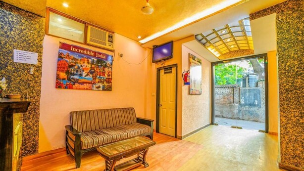 A lobby with a sofa, a television, a fire extinguisher, and a poster on the wall. - Shoba Residency  (New Delhi)