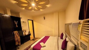 A hotel room with a bed, a ceiling fan, a heater, and a dark-colored wardrobe. - Shoba Residency  (New Delhi)